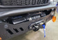 A close-up of a black winch mounted on a vehicle's front bumper, with an orange recovery hook and blue strap hanging down, set in a workshop environment.