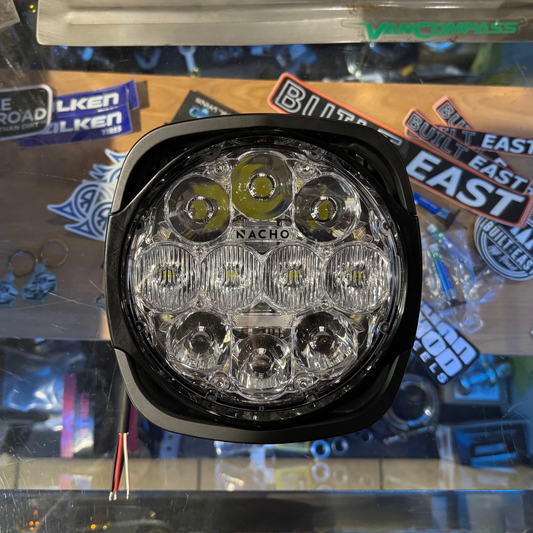 Round LED light on a reflective surface with various stickers in the background